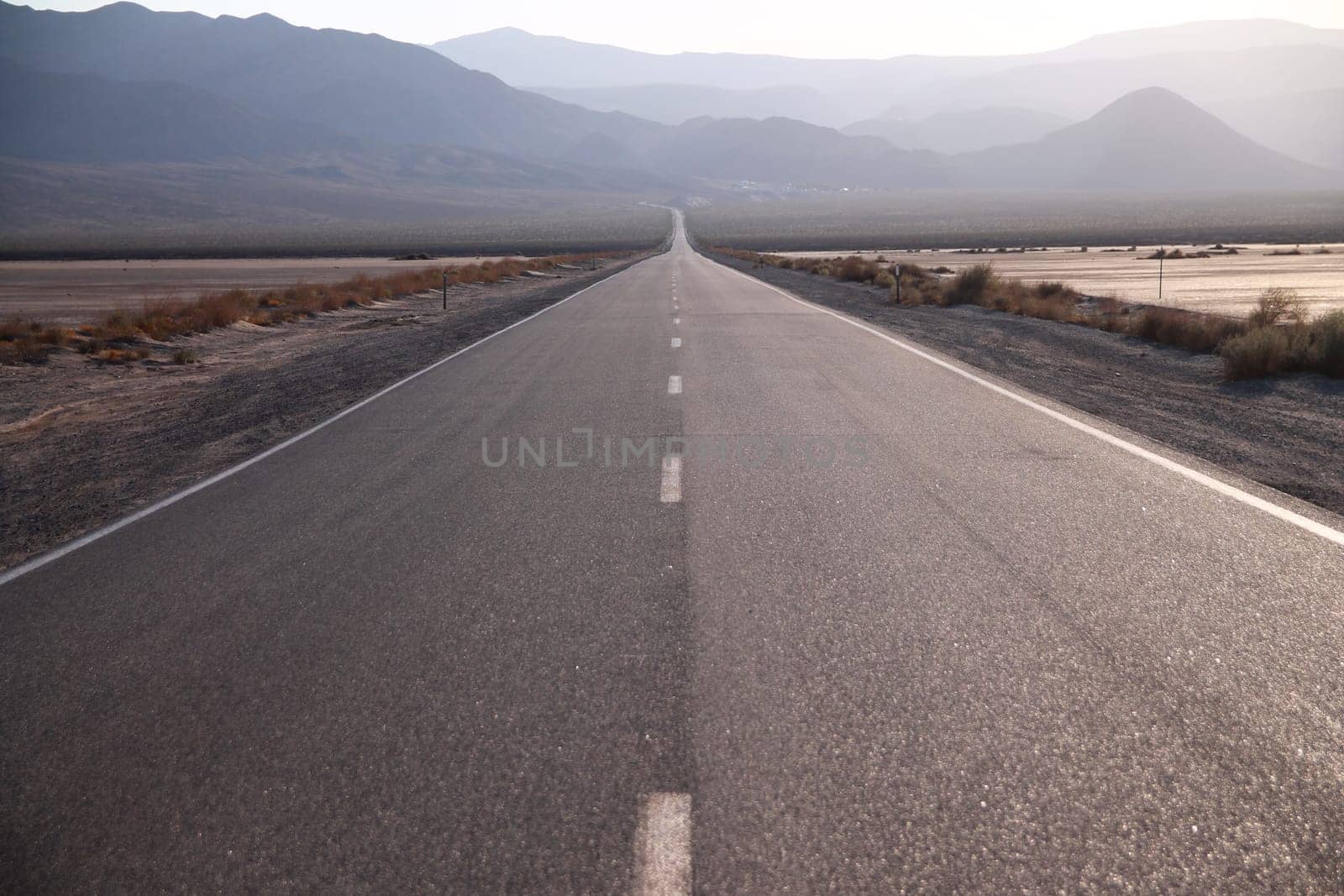 The hot sun of the Death Valley reflecting on the endless road during sunset in California