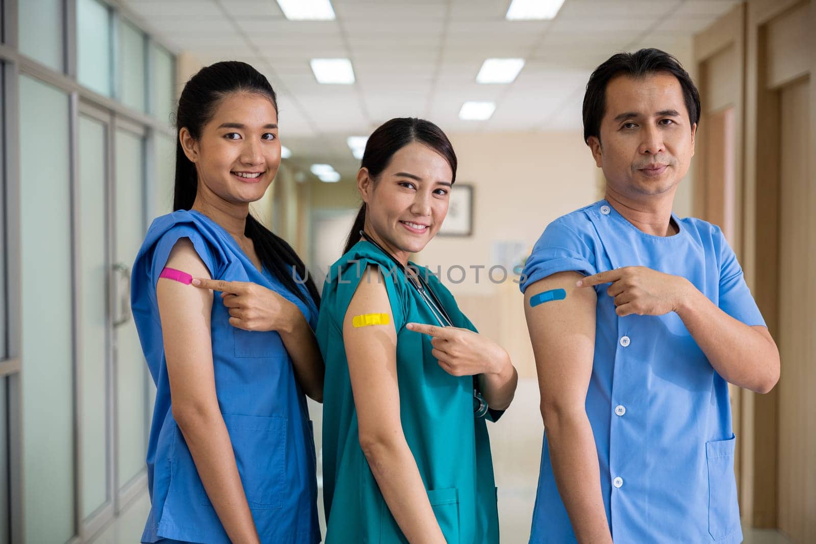 Medical personnel pointing to bandage with plaster on arm after getting against Covid-19 vaccine, happy nurse woman and man standing at hospital, Covid-19 vaccination concept