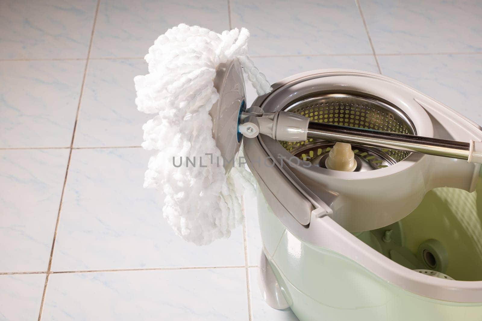 Mop with microfiber head spinning on the bucket next to floor cleaning liquid and mopping the floor house in the living room