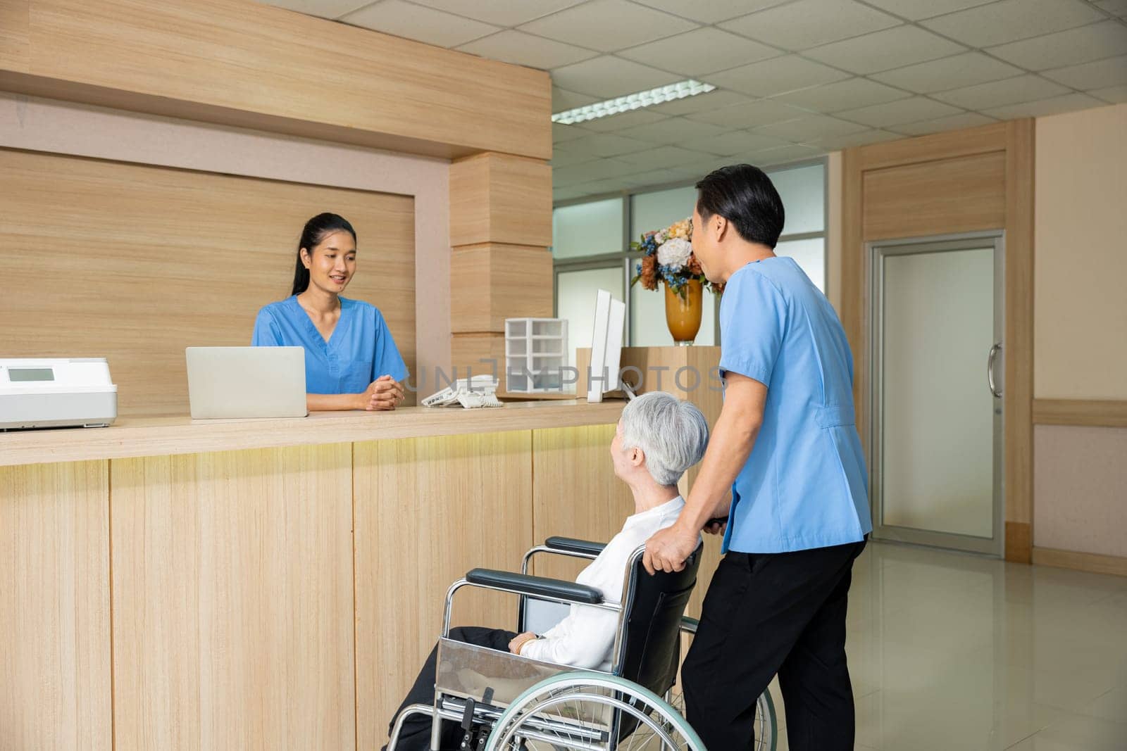 Patient elderly sit on wheelchair meet and talking with nurse or staff at front counter in of the hospital, healthcare reception service treatment process concept