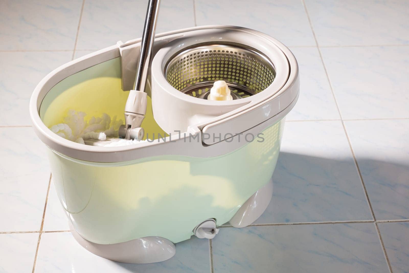 Mop with microfiber head spinning on the bucket next to floor cleaning liquid and mopping the floor house in the living room