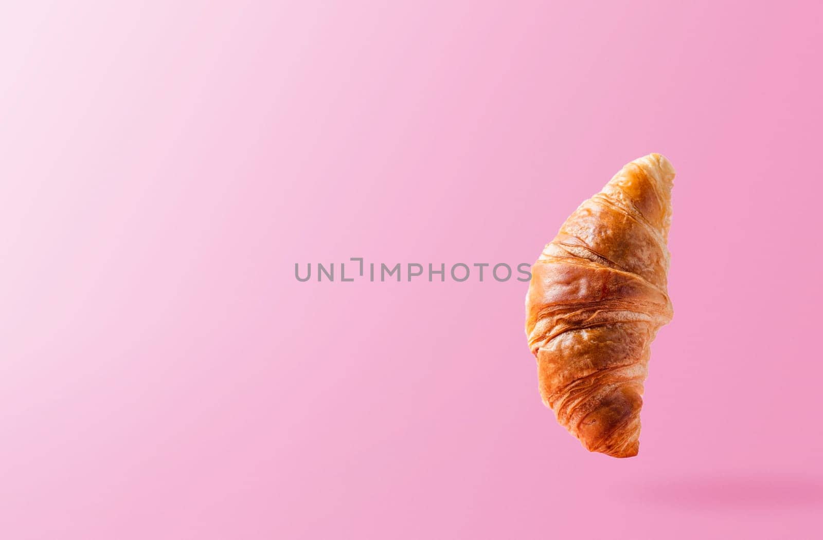 Freshly baked croissant levitating or flying. Croissant fly in the air isolated on pink background. Levitation scene. Copy space place. Signboard mockup or advertisement of bakery, confectionery