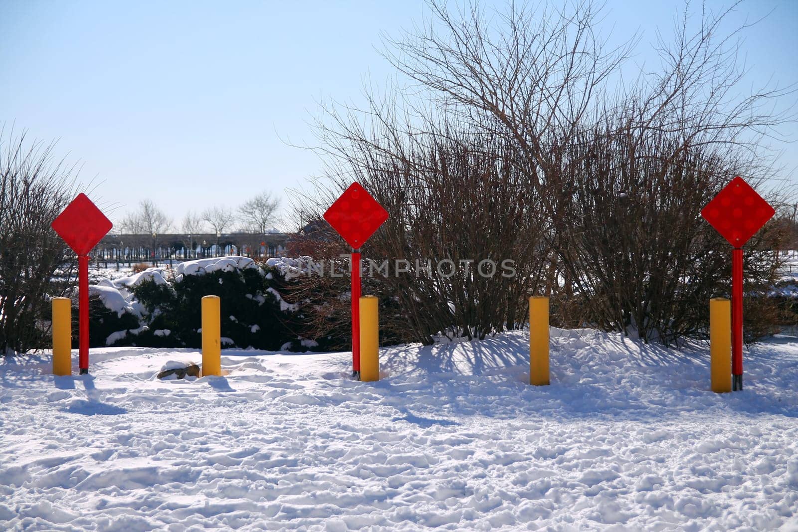 Red end of the road square sign with three yellow poles on the snow in a sunny day after a storm