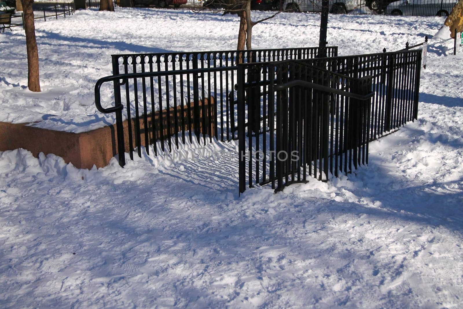 A black fence on the white snow in a park during a sunny winter day