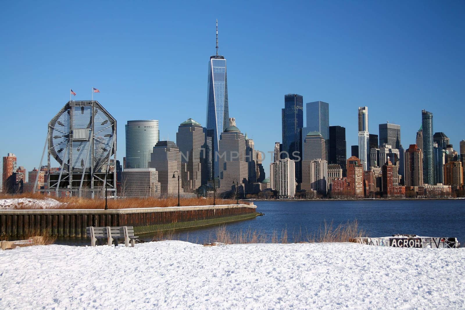 The bench and the big clock looking at downtown Manhattan with the snow on the ground from Liberty State Park in Jersey City