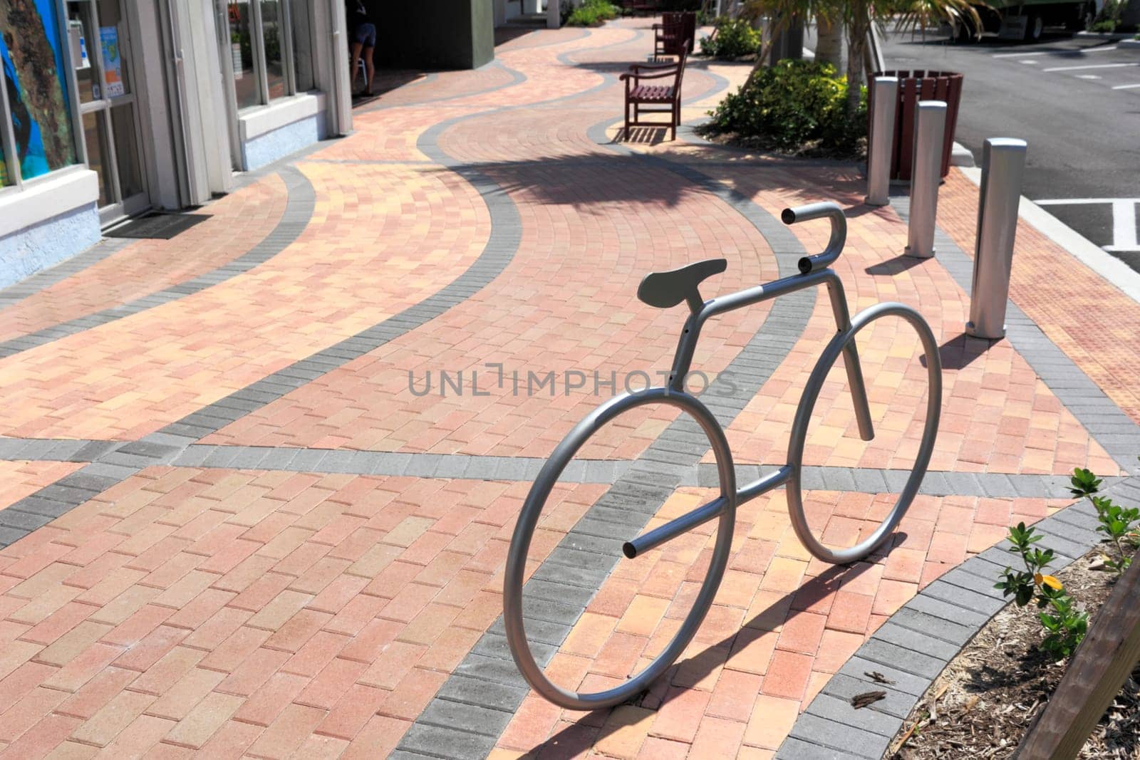 LAUDERDALE-BY-THE-SEA, FL, USA - APRIL 7, 2014: One silver metal bike rack in the shape of a bike mounted on a brick sidewalk on a sunny day. A silver bike rack in the shape of a bicycle on a brick design sidewalk with a few benches in the background.