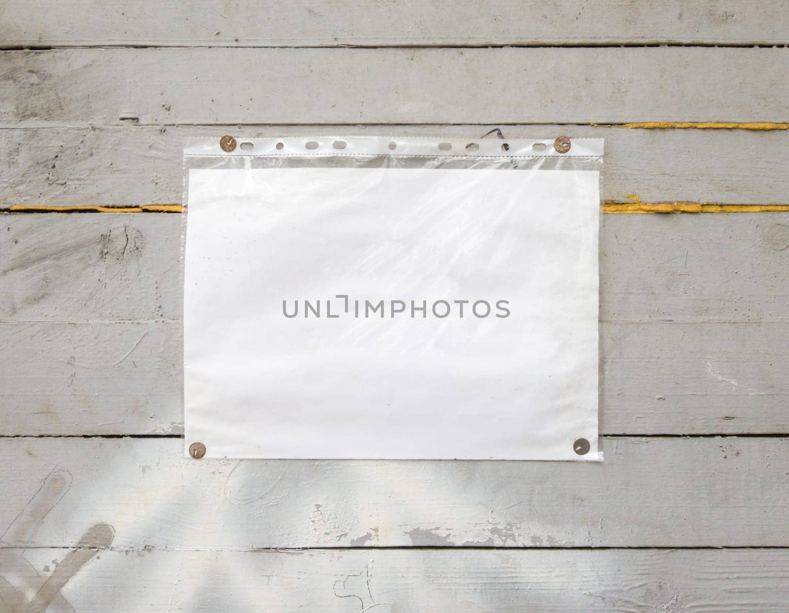 White paper sign with rivets, vintage background on a gray wooden old backdrop. Wooden textured wall, weighs a white blank cardboard sign lit by the sun, closeup.