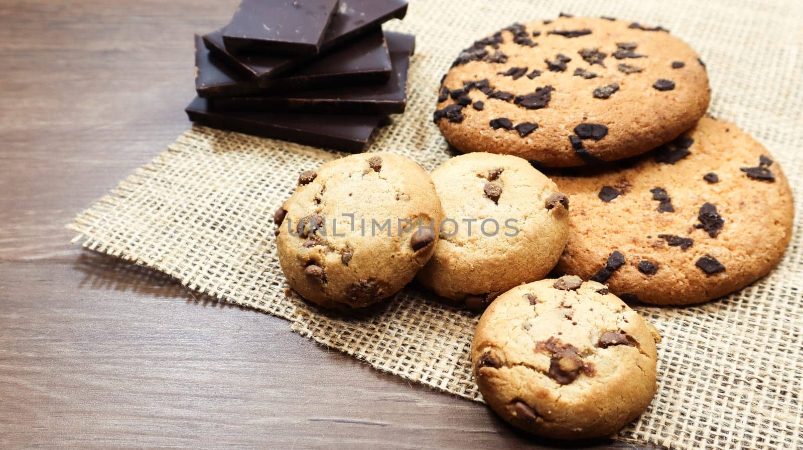 American chocolate chip cookies on a brown wooden table and on a linen napkin close-up. Traditional rounded crunchy dough with chocolate chips. Bakery. Delicious dessert, pastries. Rural still life