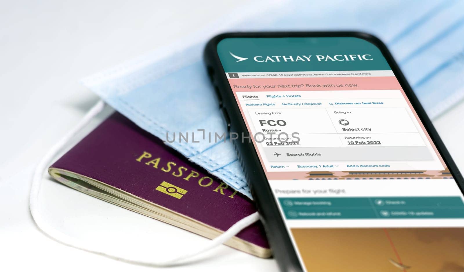 Rome, Italy, July 2021: phone with the Cathay Pacific airlines app on the screen lying over a protective mask and a passport. Travel safety and restrictions during coronavirus pandemic