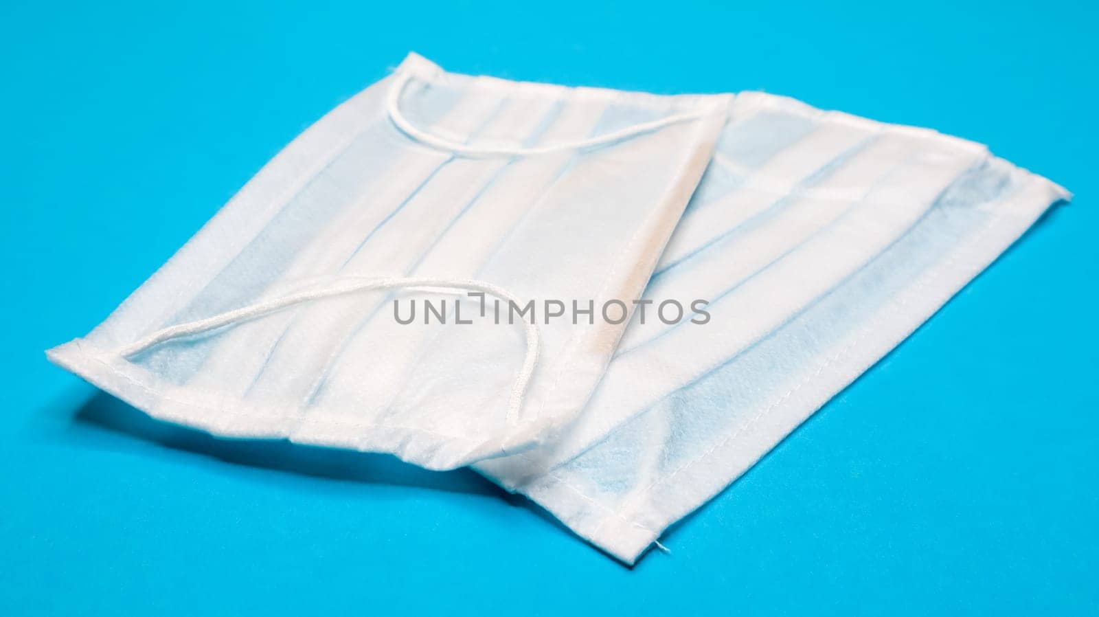 Two three-layer disposable surgical face masks with rubber pads to cover the mouth and nose against a blue background. The concept of protection from bacteria, healthcare and medicine. COVID-19