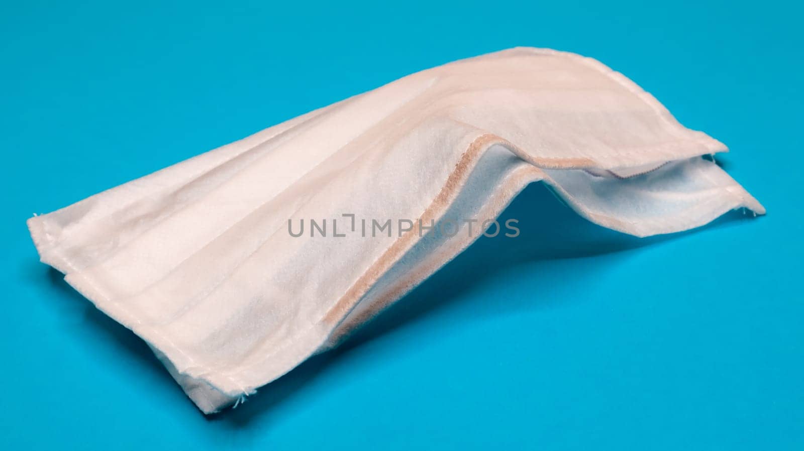 Two three-layer disposable surgical face masks with rubber pads to cover the mouth and nose against a blue background. The concept of protection from bacteria, healthcare and medicine. COVID-19.