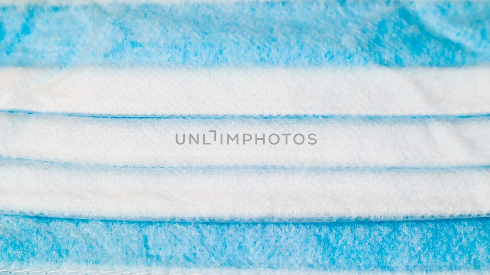 One 3-ply disposable surgical face mask close-up with rubber pads covering mouth and nose against blue background. The concept of protection from bacteria, healthcare and medicine. COVID-19
