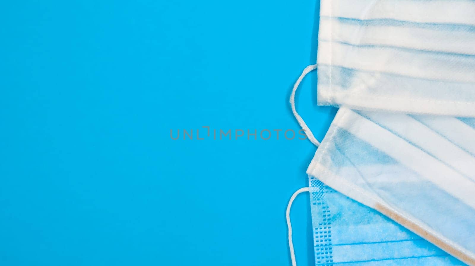 Three disposable surgical face masks with rubber pads to cover the mouth and nose on a blue background. The concept of protection from bacteria, healthcare and medicine. COVID-19. Copy space.