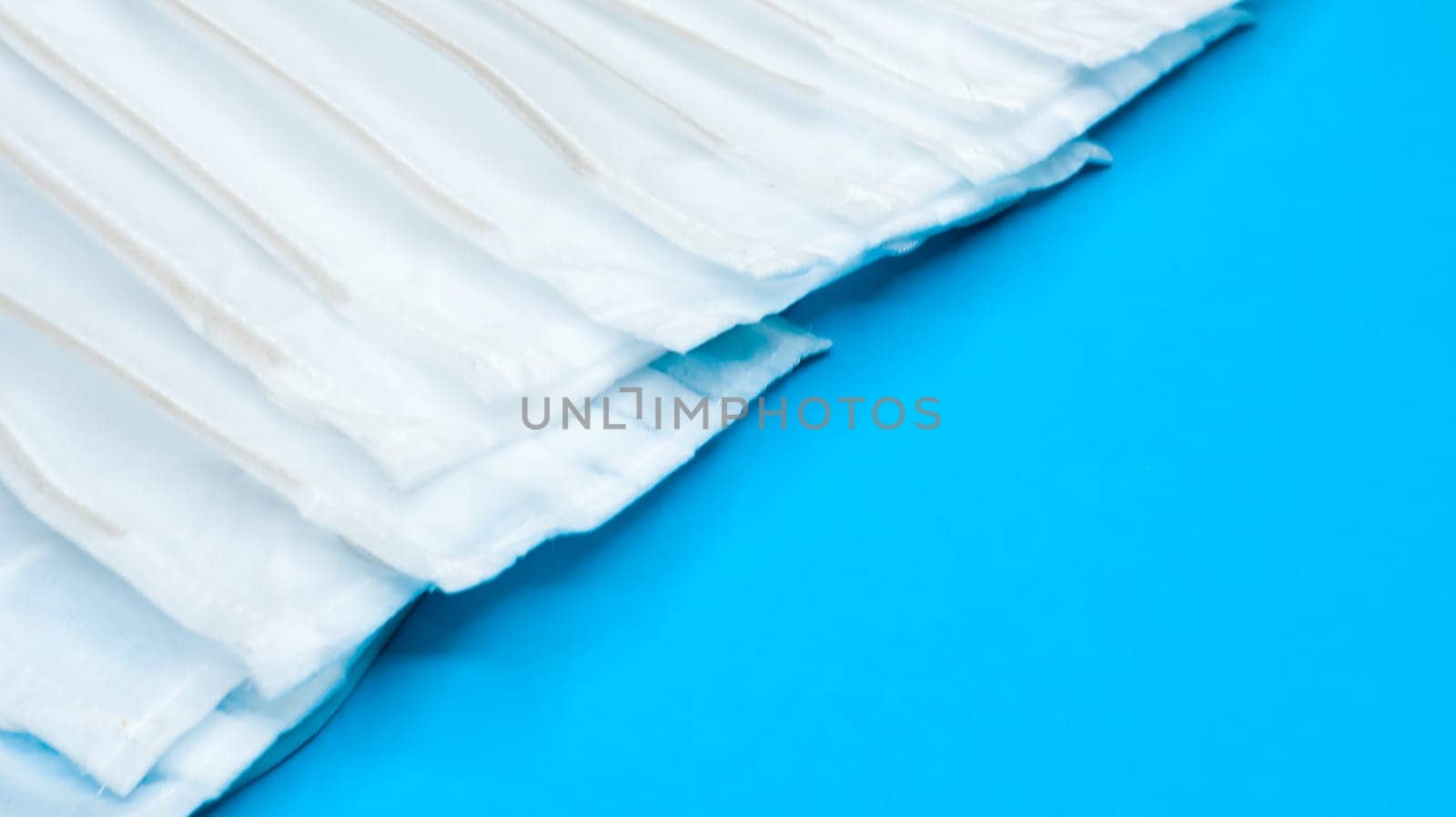 Many antiviral protective medical face masks with earloops are set against a blue background. Surgical mask background. Respiratory syndrome, coronavirus disease COVID-19. Copy space.