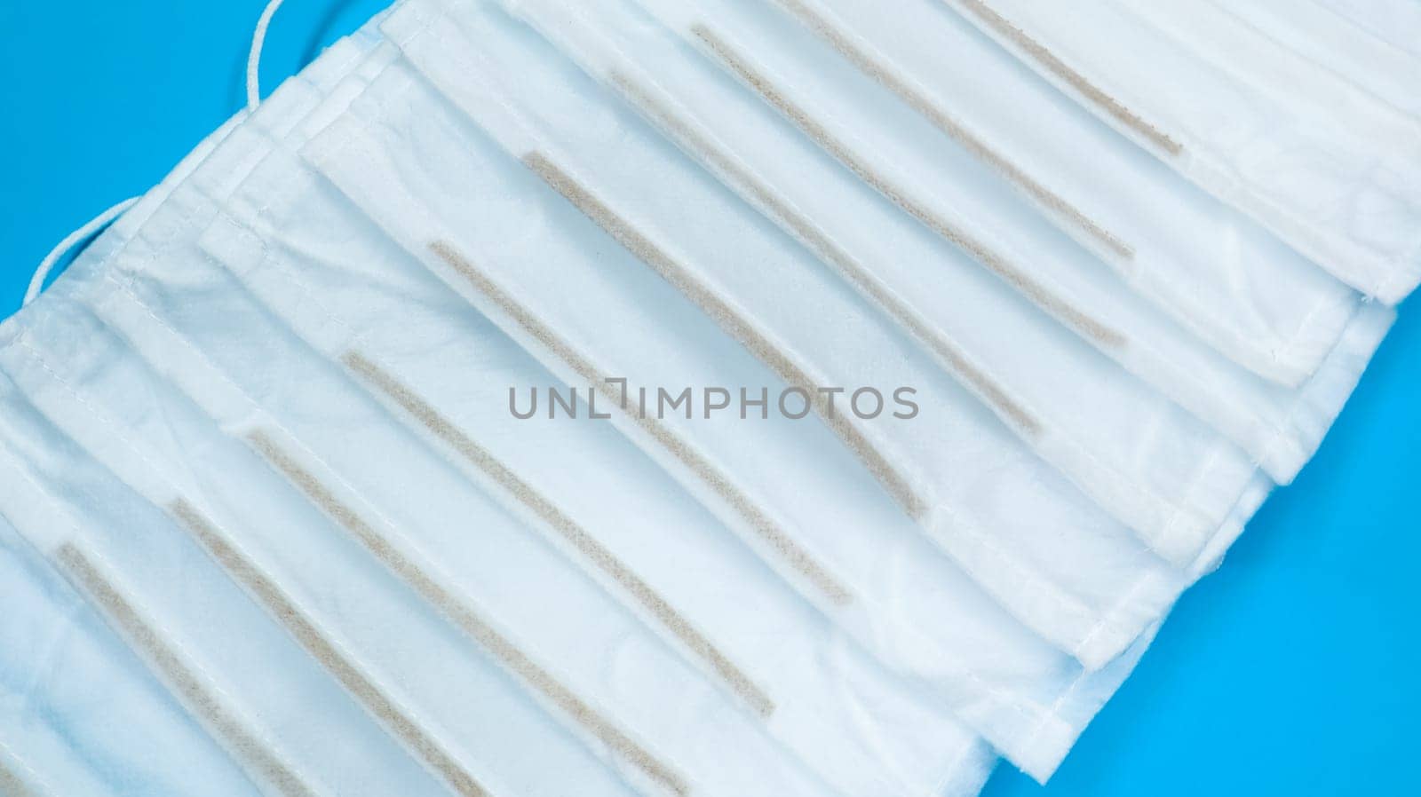 Coronavirus protection. Many antiviral protective medical face masks with ear loops spread out on a blue background. Surgical mask background. Respiratory syndrome, coronavirus disease COVID-19