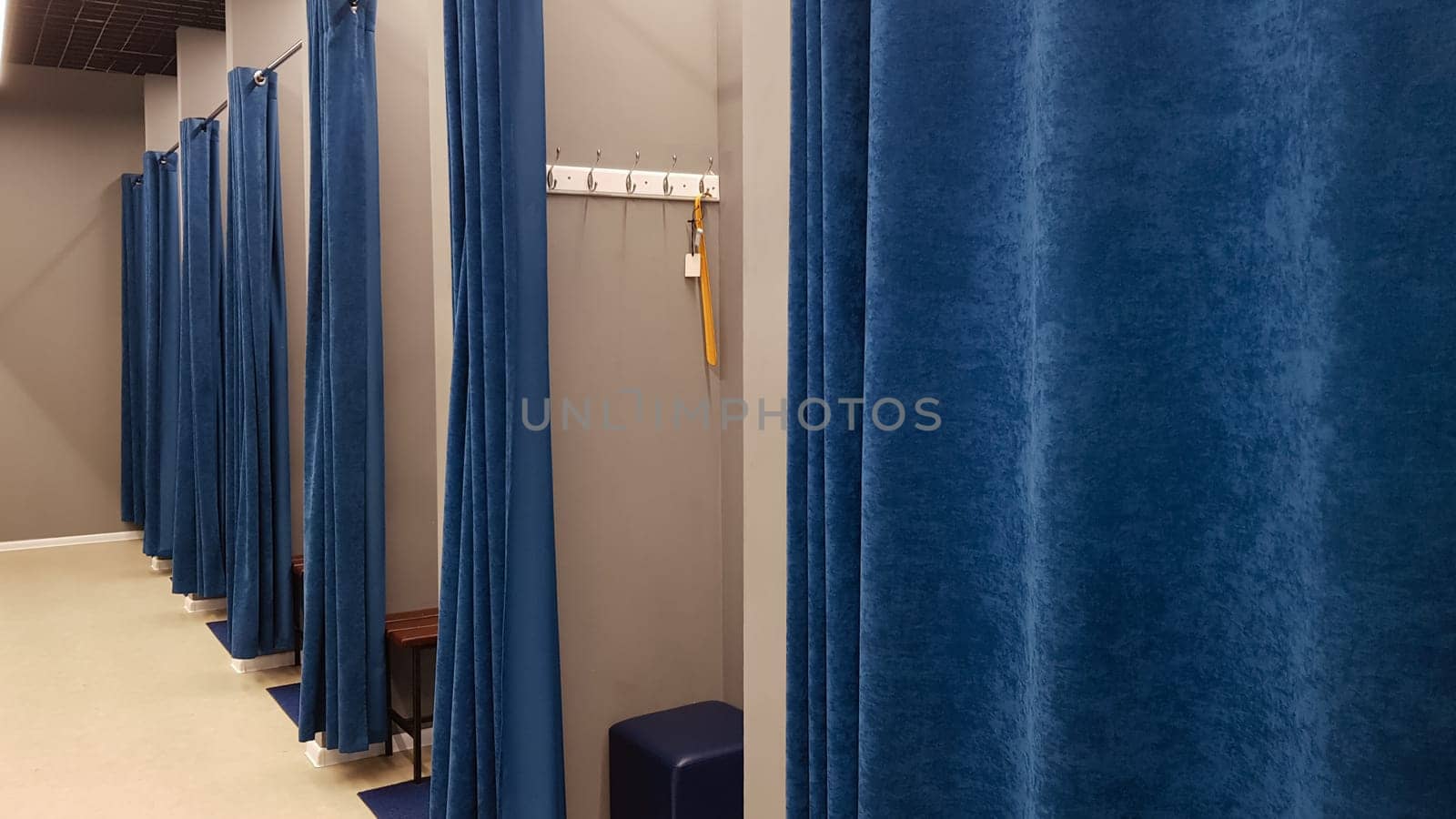 Boutique interior, fitting room in a shopping center. Nobody. Empty fitting rooms with blue curtains and gray walls and a large mirror. Dressing rooms in a clothing store without people
