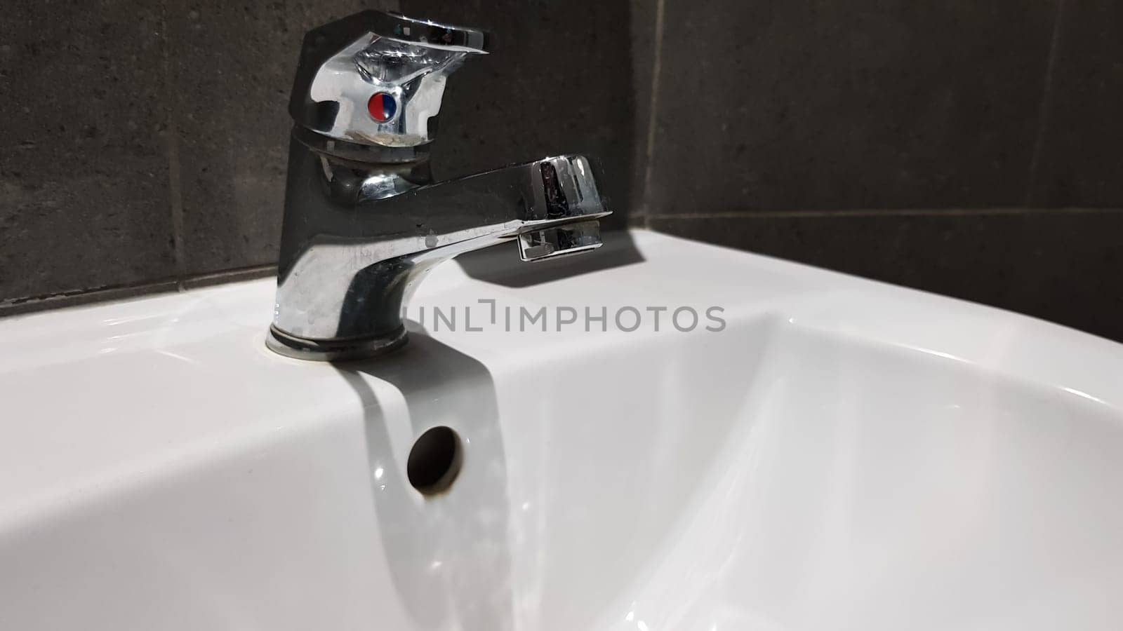 white ceramic washbasin with chrome faucet in the toilet with gray tile.