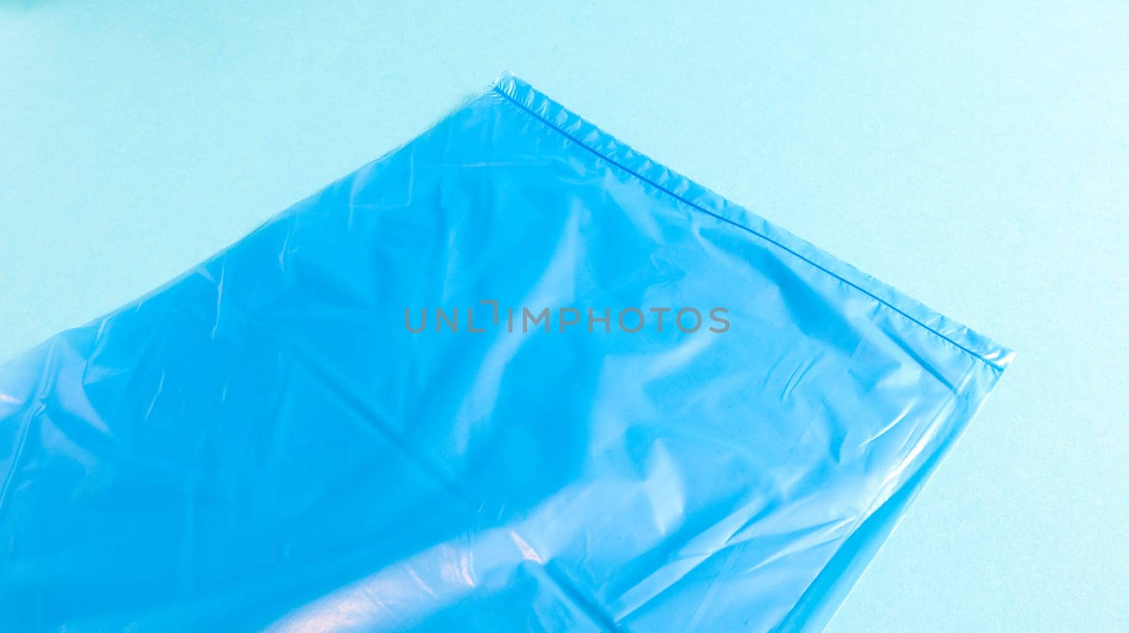 One torn plastic garbage bag in blue on a blue background. A bag that is designed to accommodate garbage in it and is used at home and placed in various garbage containers