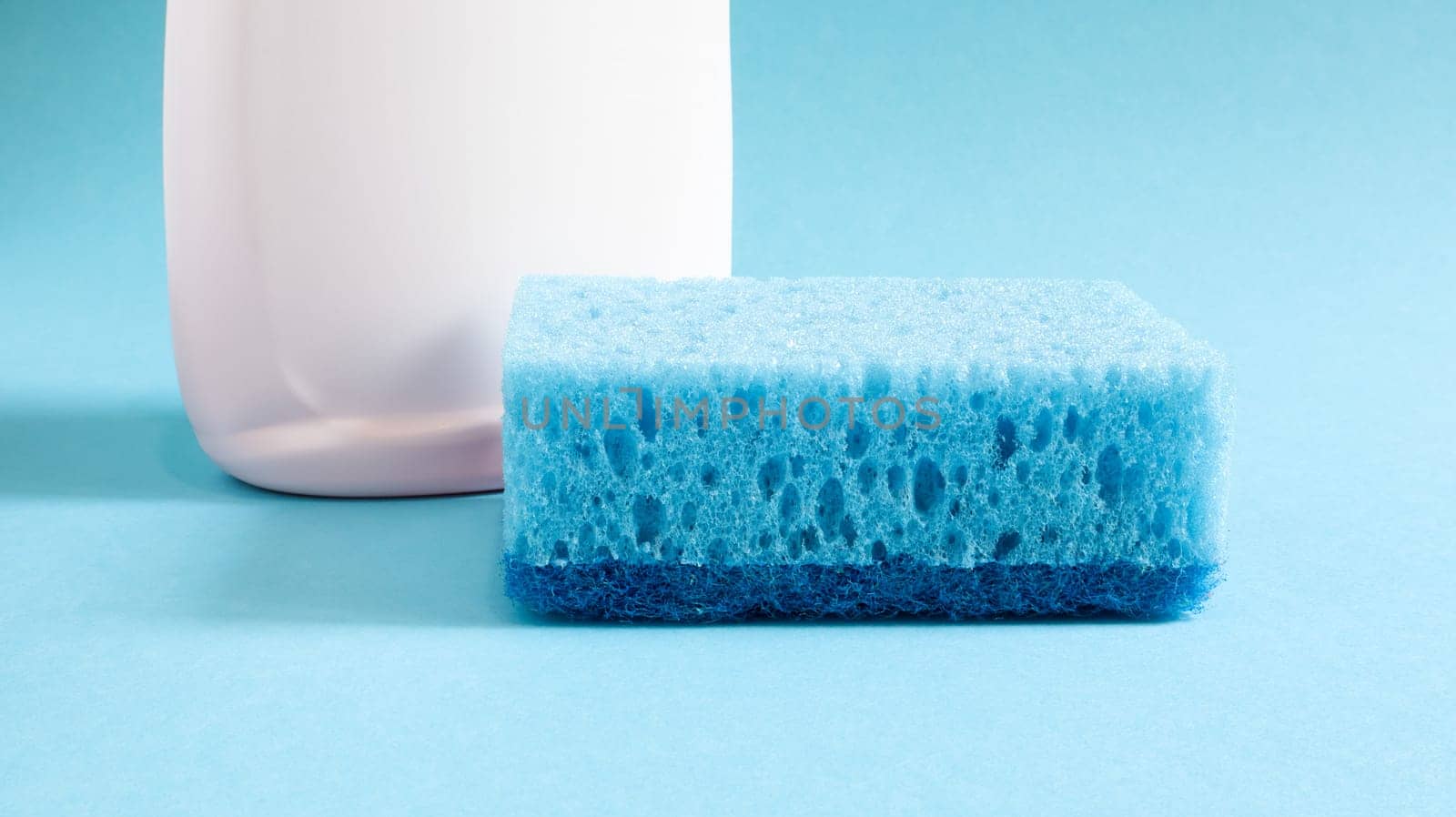 One blue sponge with a white bottle of detergent on a blue background. Convenience of sponges consists in good detergent retention that allows to use it economically.