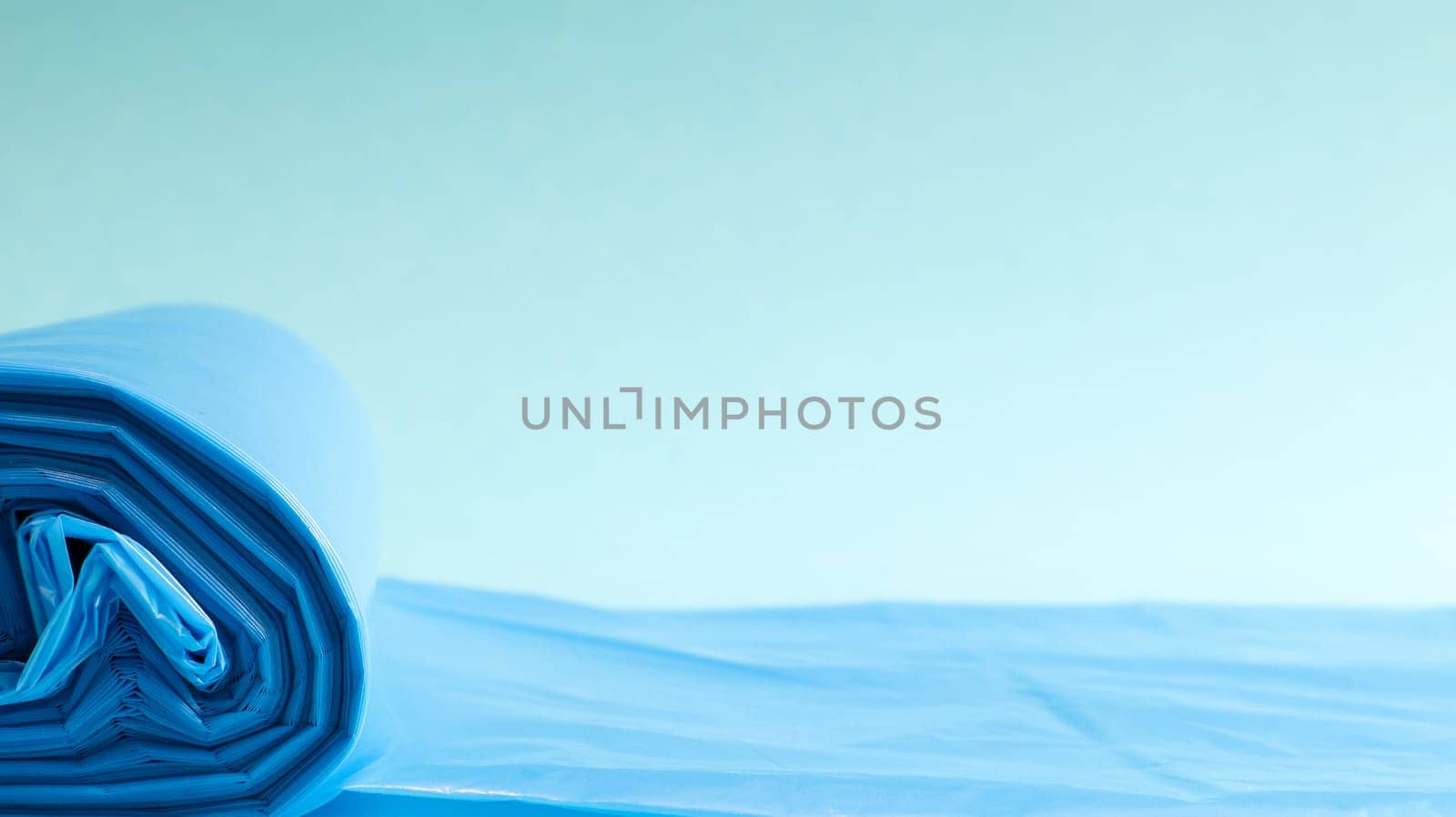 One roll of plastic trash bags in blue on a blue background. Bags that are designed to accommodate garbage in them and used at home and placed in various garbage containers. Copy space.