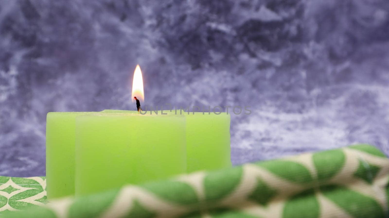 Composition with one green lit candle on a table with a green linen napkin against a beautiful gray marble background. Place for your text. Christmas decorations