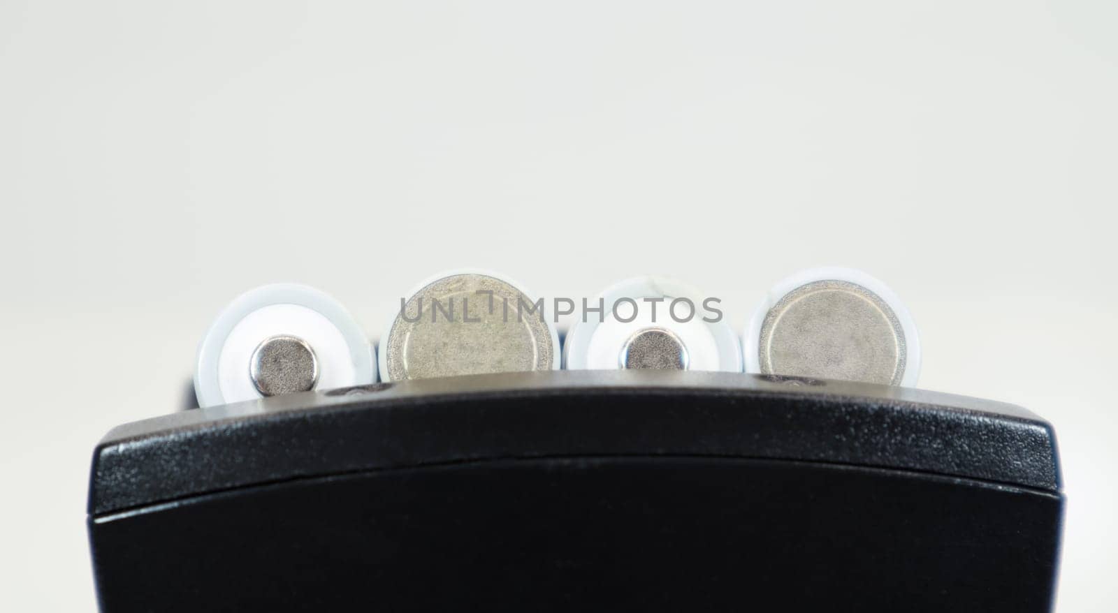 Fast charging of AA batteries. Rechargeable batteries in a black charger with four battery cells on a white background