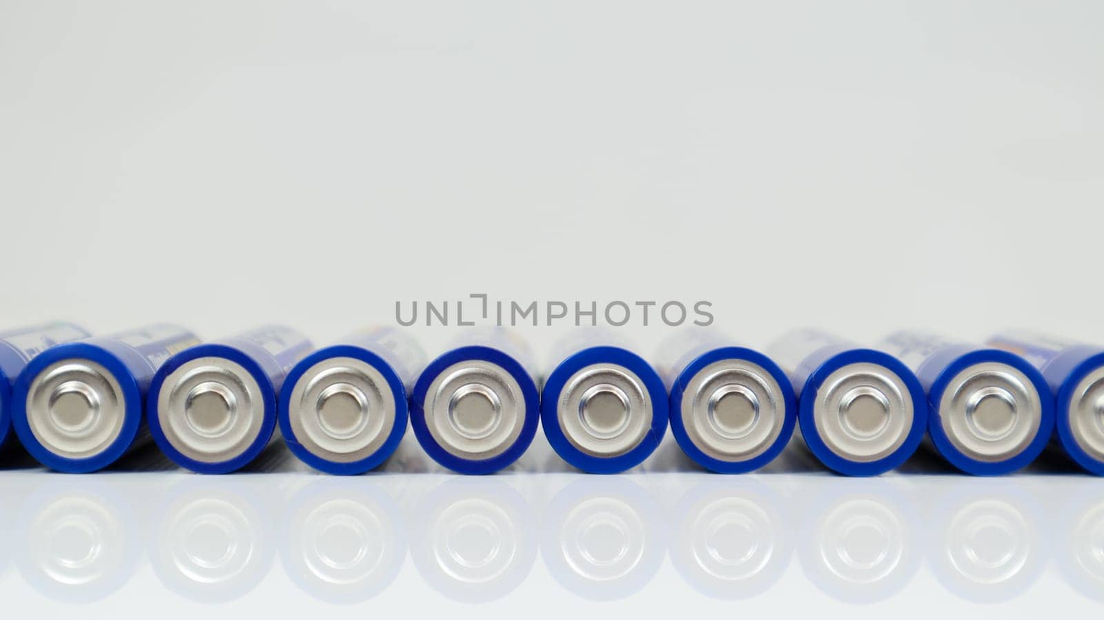Lots of AA alkaline batteries on a white glossy background with reflection with copy space lined up in one line