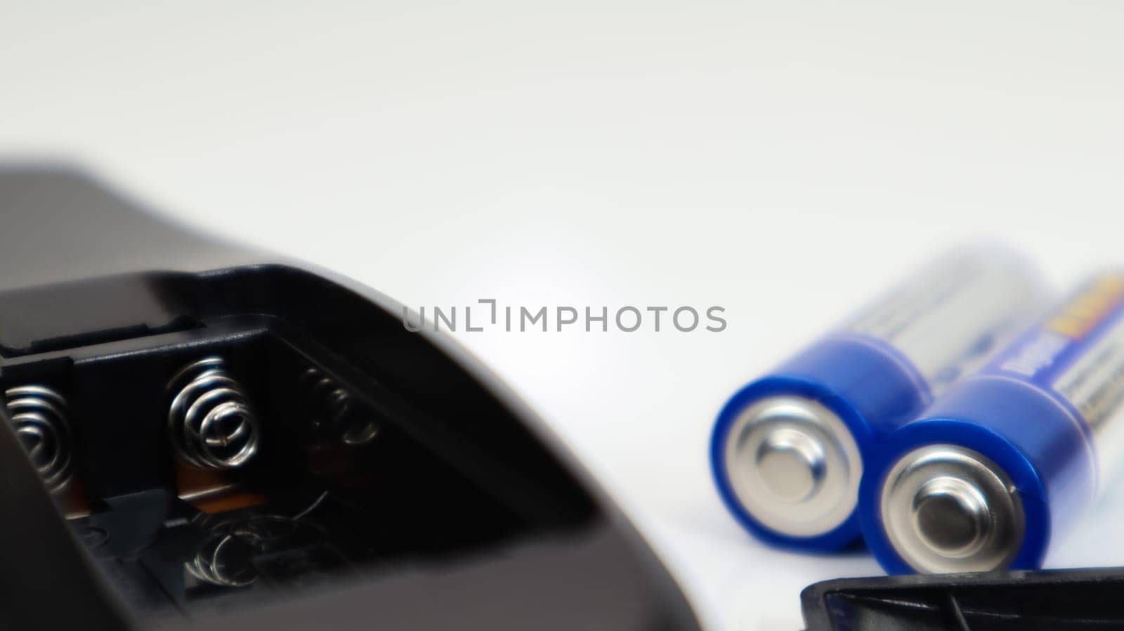 Black remote control with blue AAA batteries on a white background. Battery replacement, spare parts. Battery empty compartment of the remote control close-up