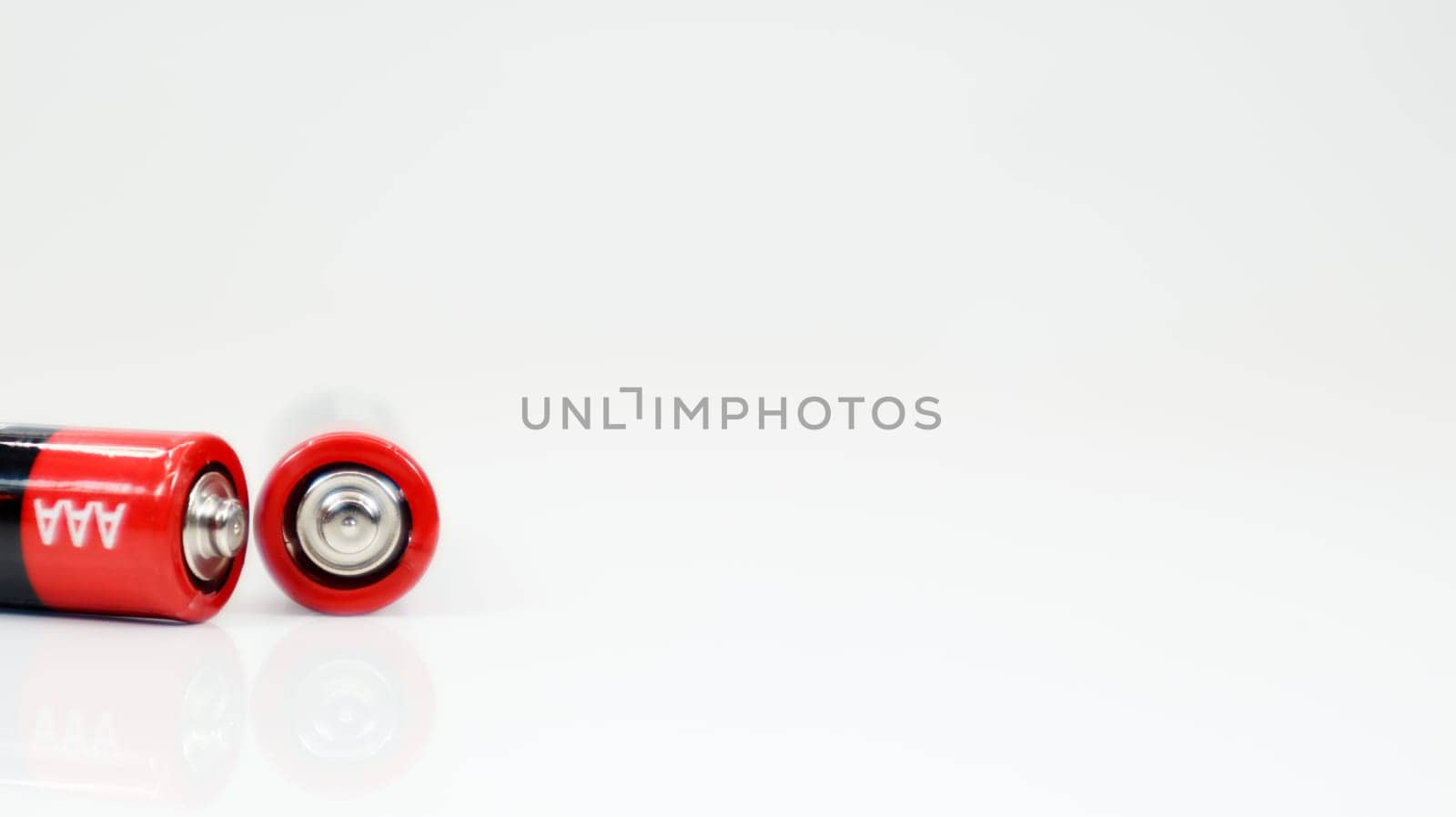 Two type AAA alkaline rechargeable batteries on white glossy background with reflection with copy space