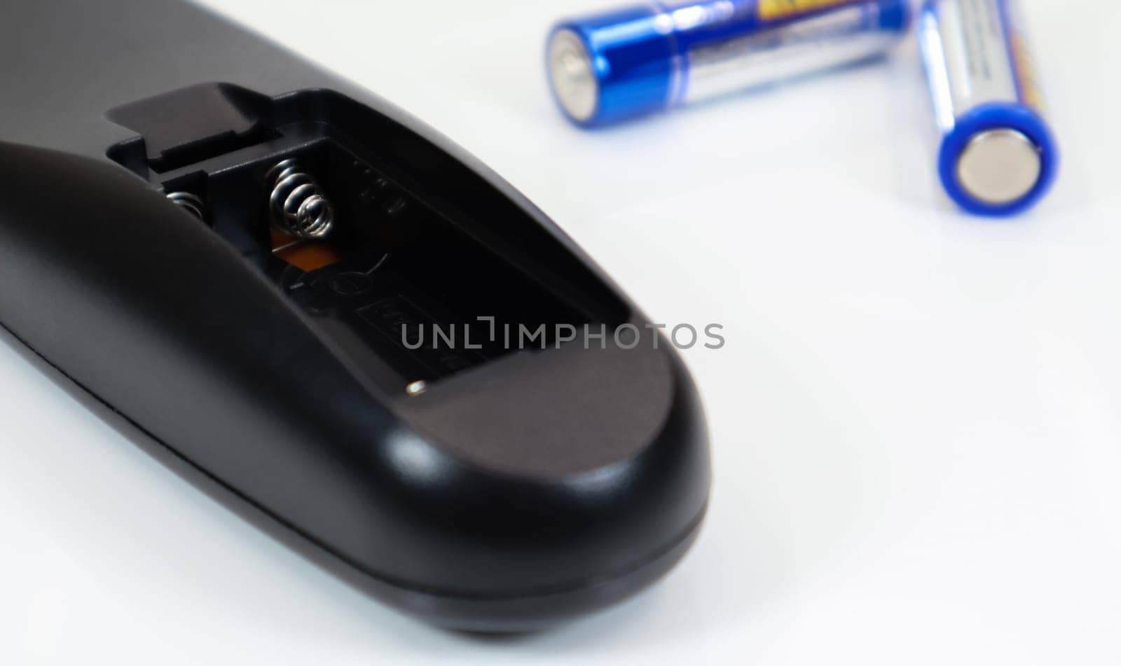 Black remote control with blue AAA batteries on a white background. Battery replacement, spare parts. Battery empty compartment of the remote control close-up