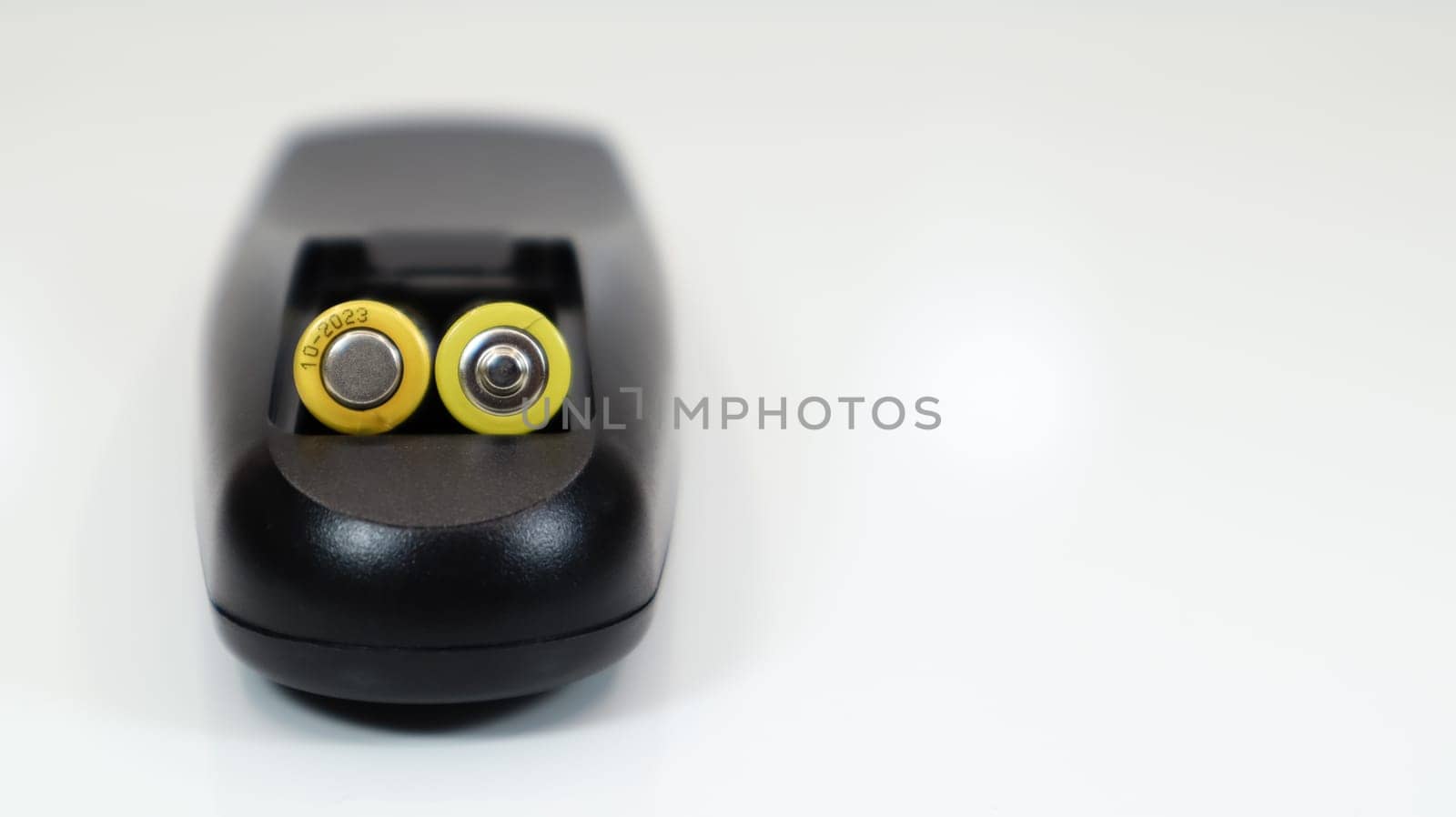 Black remote control with yellow AAA batteries on a white background. Battery replacement, spare parts. Remote control battery compartment close-up. Copy space.