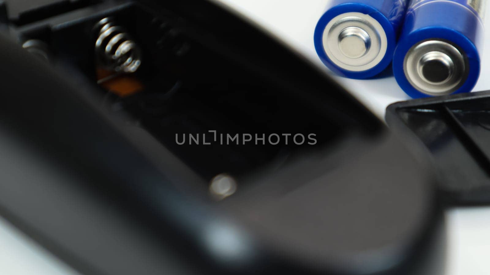 Black remote control with blue AAA batteries on a white background. Battery replacement, spare parts. Battery empty compartment of the remote control close-up