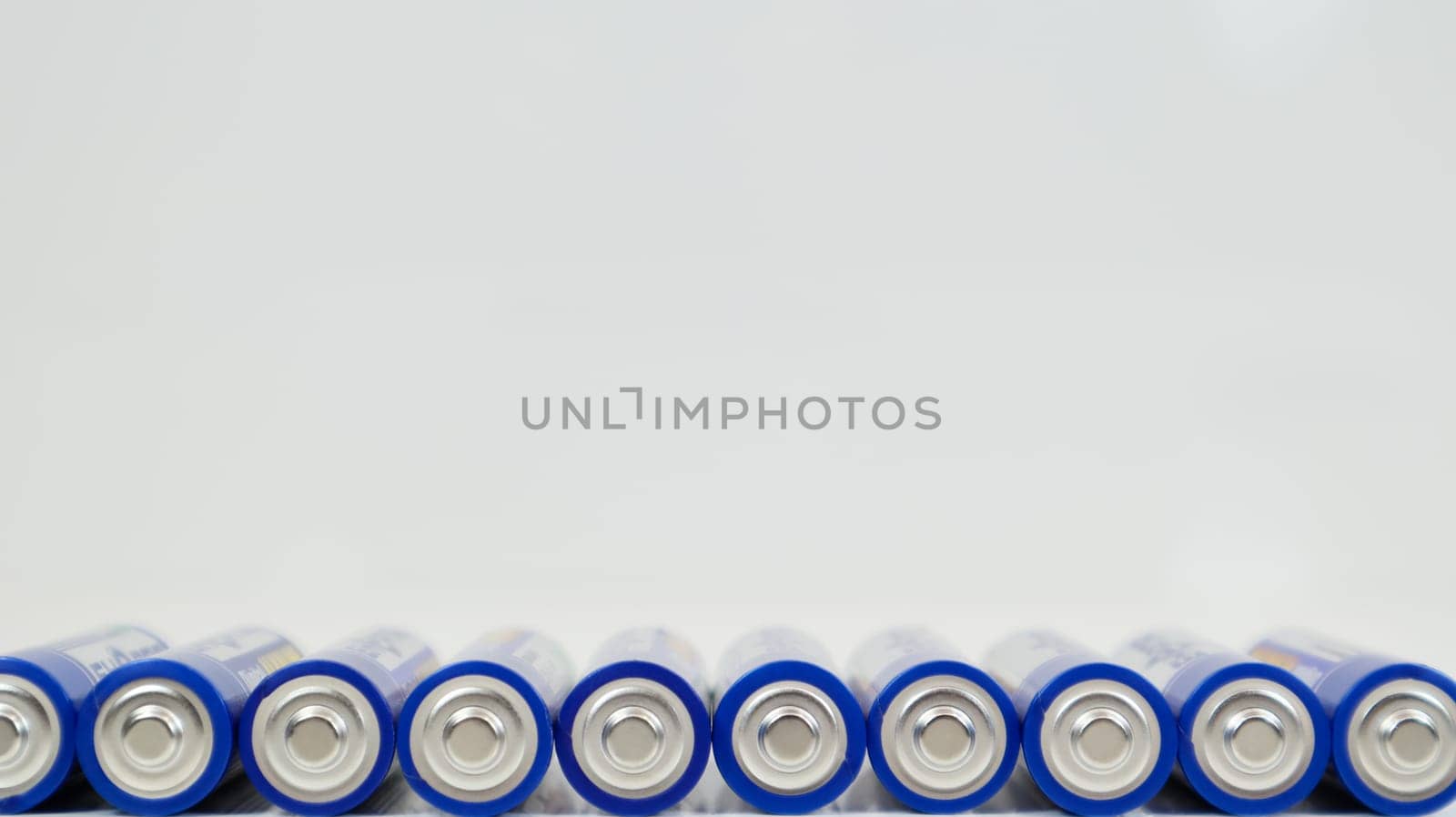 Lots of AA alkaline batteries on a white glossy background with reflection with copy space lined up in one line. Ukraine, Kiev - January 7, 2021