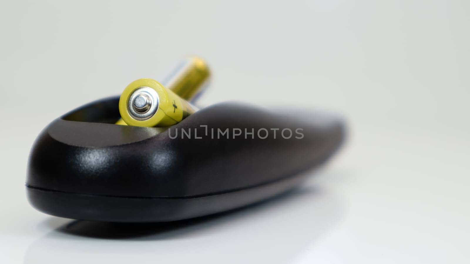 Black remote control with yellow AAA batteries on a white background. Battery replacement, spare parts. Remote control battery compartment close-up