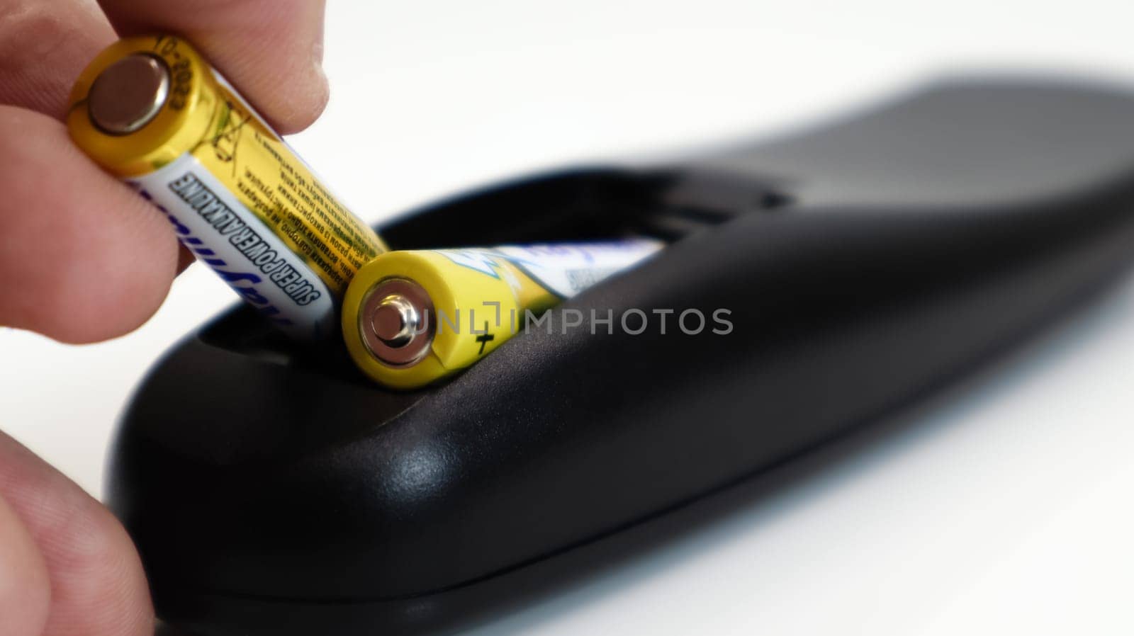 Insert the AAA size battery into the remote control. Installing batteries in the wireless device. A male hand holds a yellow alkaline battery. Text in English and Russian