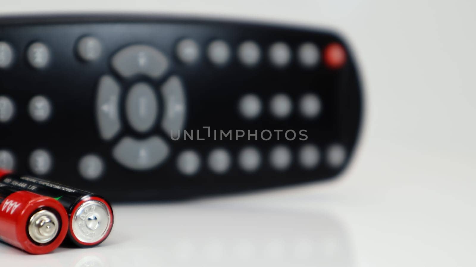 Black TV remote control with AAA alkaline batteries in red and white on a white background. Battery replacement, spare parts. Remote control battery compartment close-up