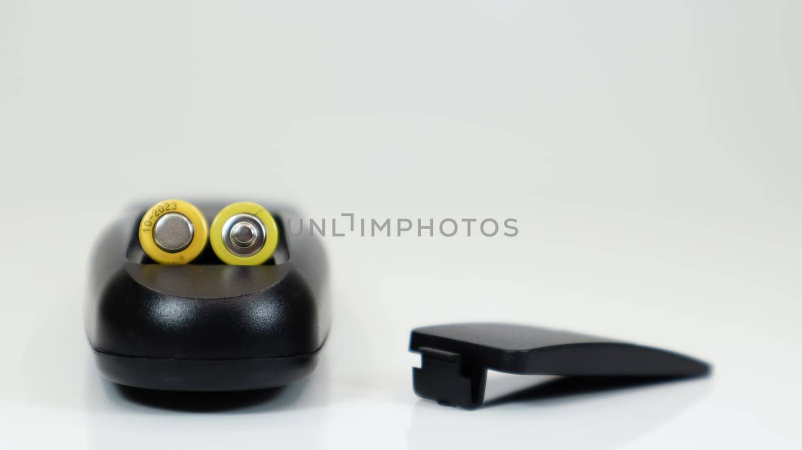 Black remote control with yellow AAA batteries on a white background. Battery replacement, spare parts. Remote control battery compartment close-up