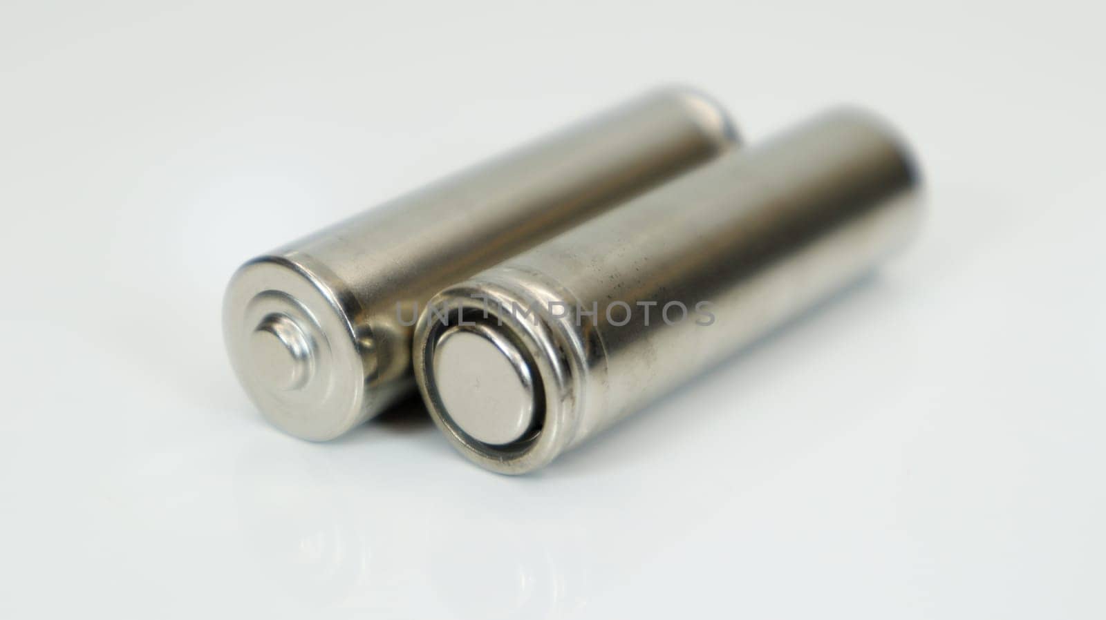 AA alkaline rechargeable batteries on white glossy background with reflection. Close up two empty batteries with copy space