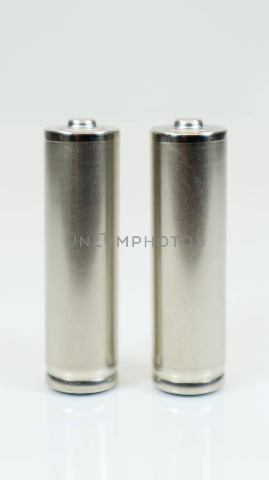 AA alkaline rechargeable batteries on white glossy background with reflection. Close up two empty batteries with copy space. Vertical photography