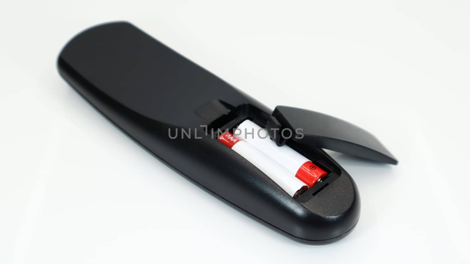 Black TV remote control with AAA alkaline batteries in red and white on a white background. Battery replacement, spare parts. Remote control battery compartment close-up