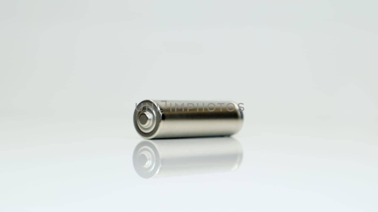 AA alkaline rechargeable battery on white glossy background with reflection. Close one empty battery with copy space