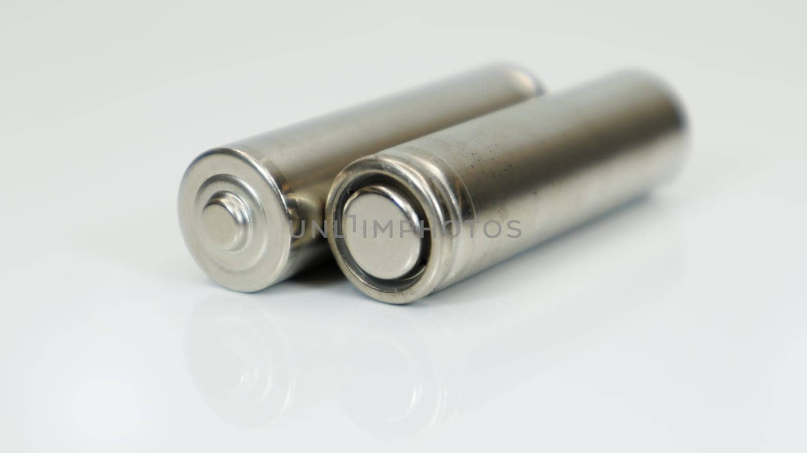 AA alkaline rechargeable batteries on white glossy background with reflection. Close up two empty batteries with copy space