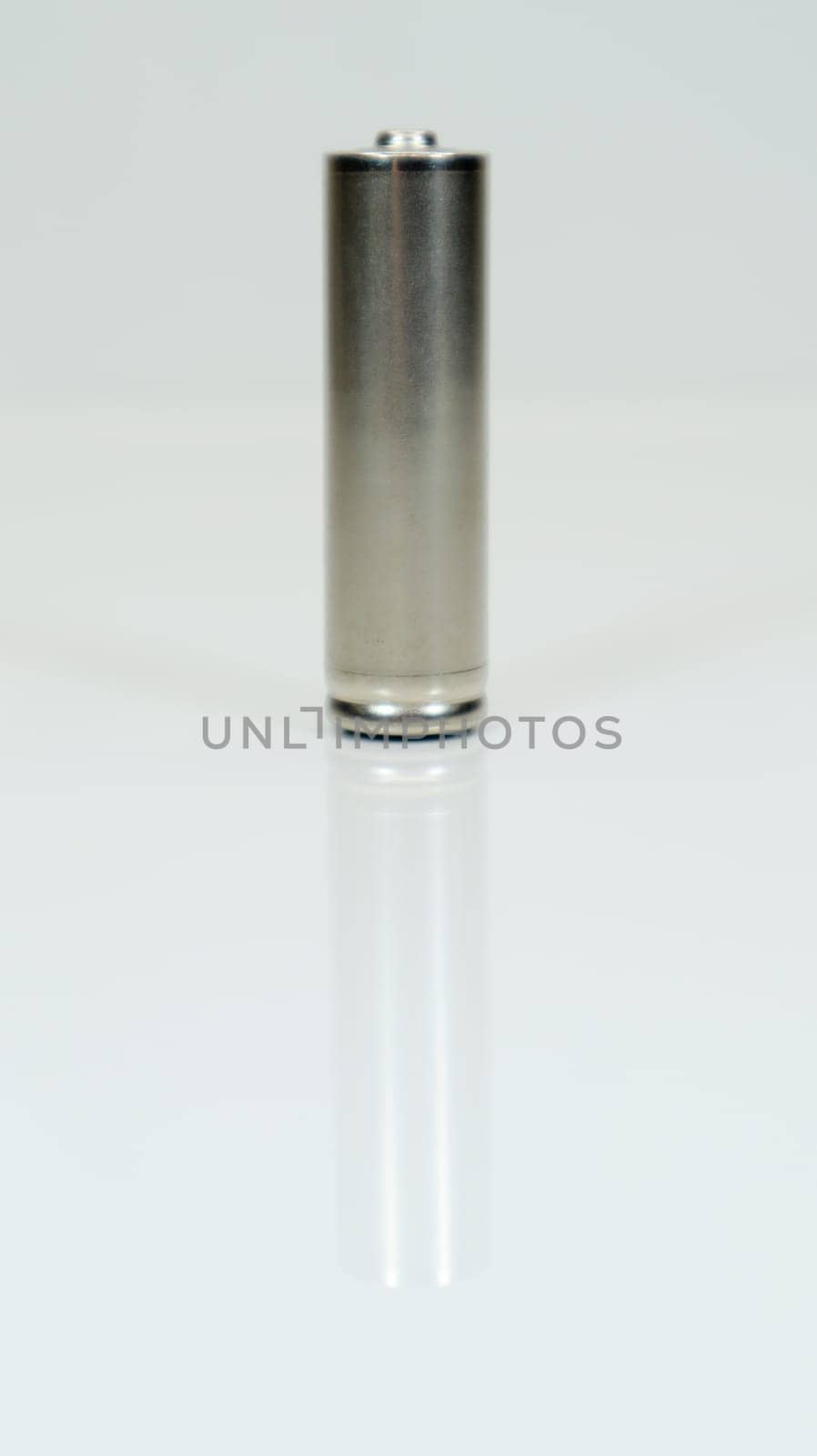 AA alkaline rechargeable battery on white glossy background with reflection. Close one empty battery with copy space. Vertical photography