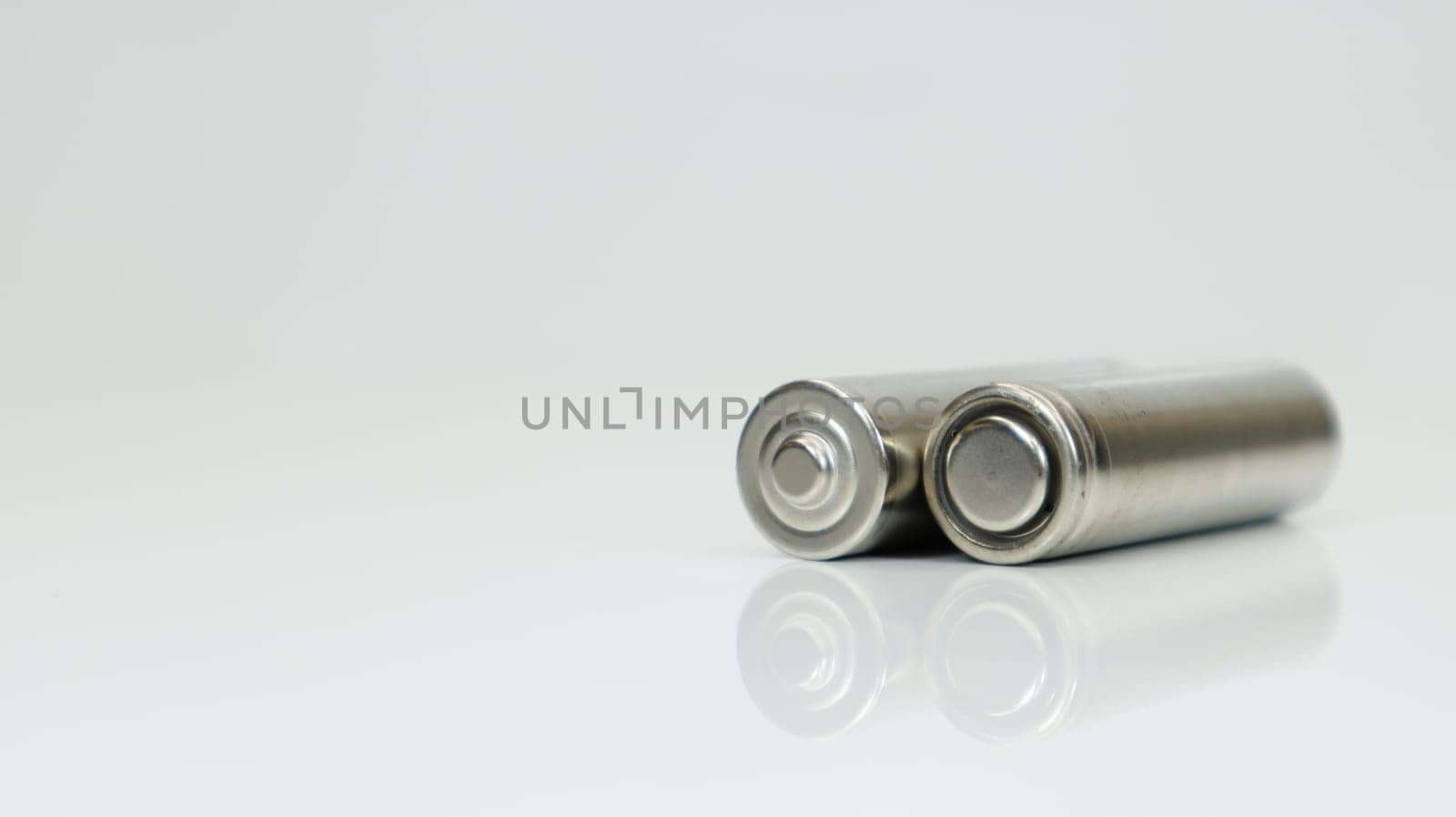 AA alkaline rechargeable batteries on white glossy background with reflection. Close up two empty batteries with copy space