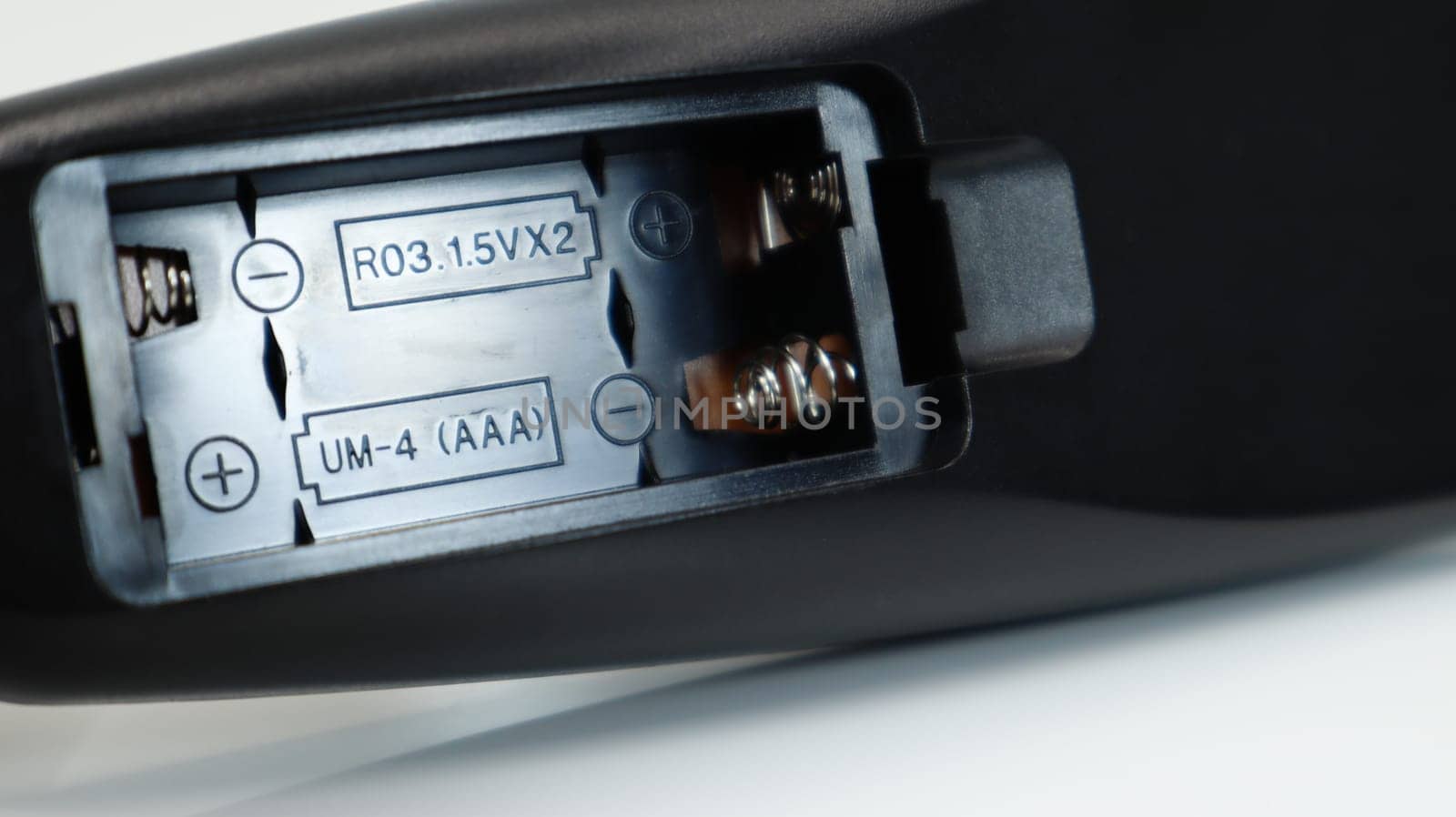 Black TV remote control with AAA alkaline batteries on a white background. Battery replacement, spare parts. Close up of an empty battery compartment of the remote control