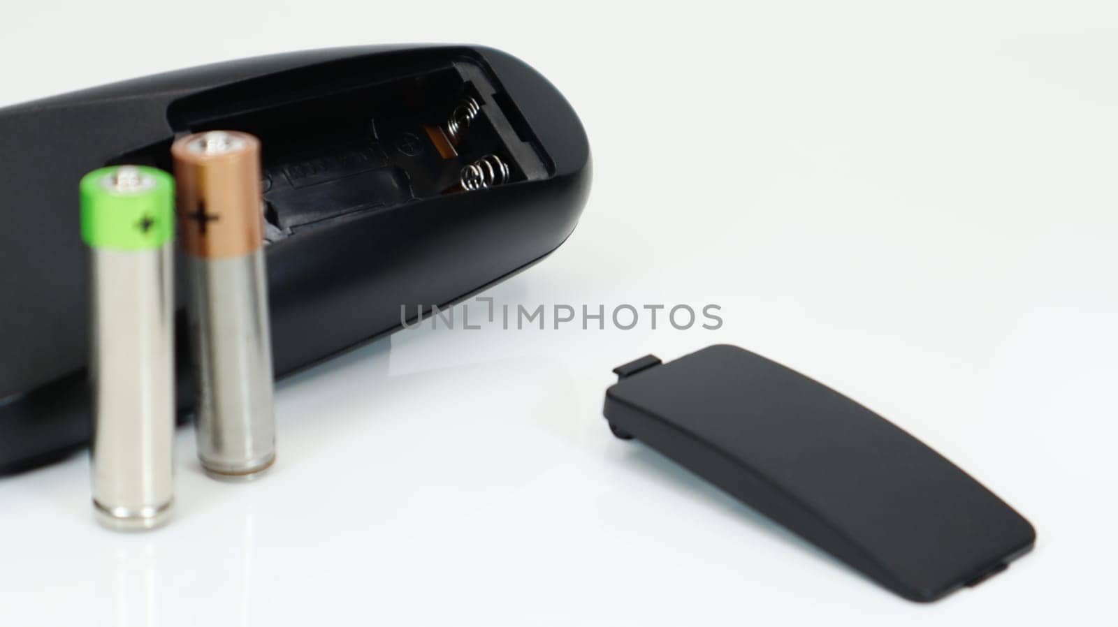 Black TV remote control with AAA alkaline batteries on a white background. Battery replacement, spare parts. Close up of an empty battery compartment of the remote control