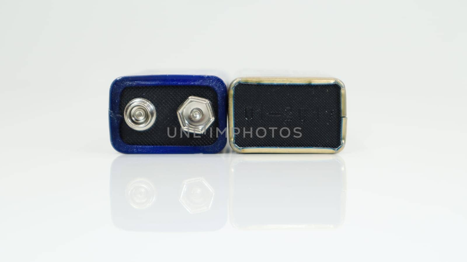 Two blue used PP3 batteries on a white background with reflection. Main battery for personal power supplies. Close-up of a scratched and used battery connector