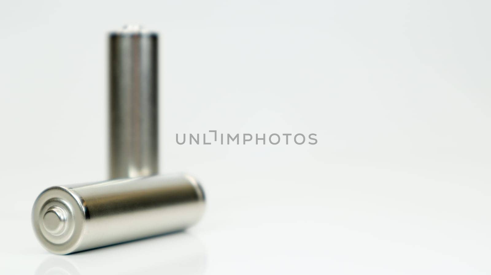 AA alkaline rechargeable batteries on white glossy background with reflection. Close up two empty batteries with copy space