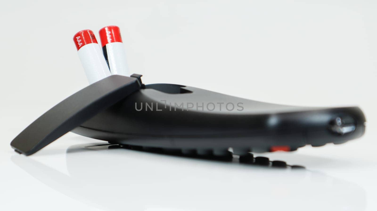 Black TV remote control with AAA alkaline batteries on a white background. Battery replacement, spare parts. Close up of the battery compartment of the remote control