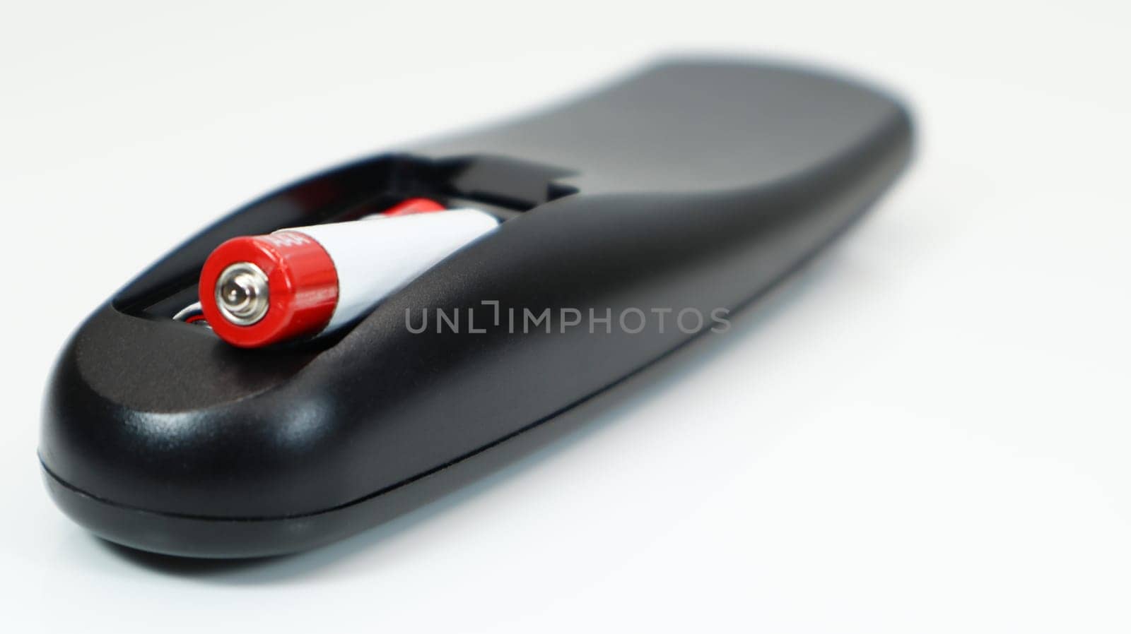 Black TV remote control with AAA alkaline batteries on a white background. Battery replacement, spare parts. Close up of the battery compartment of the remote control